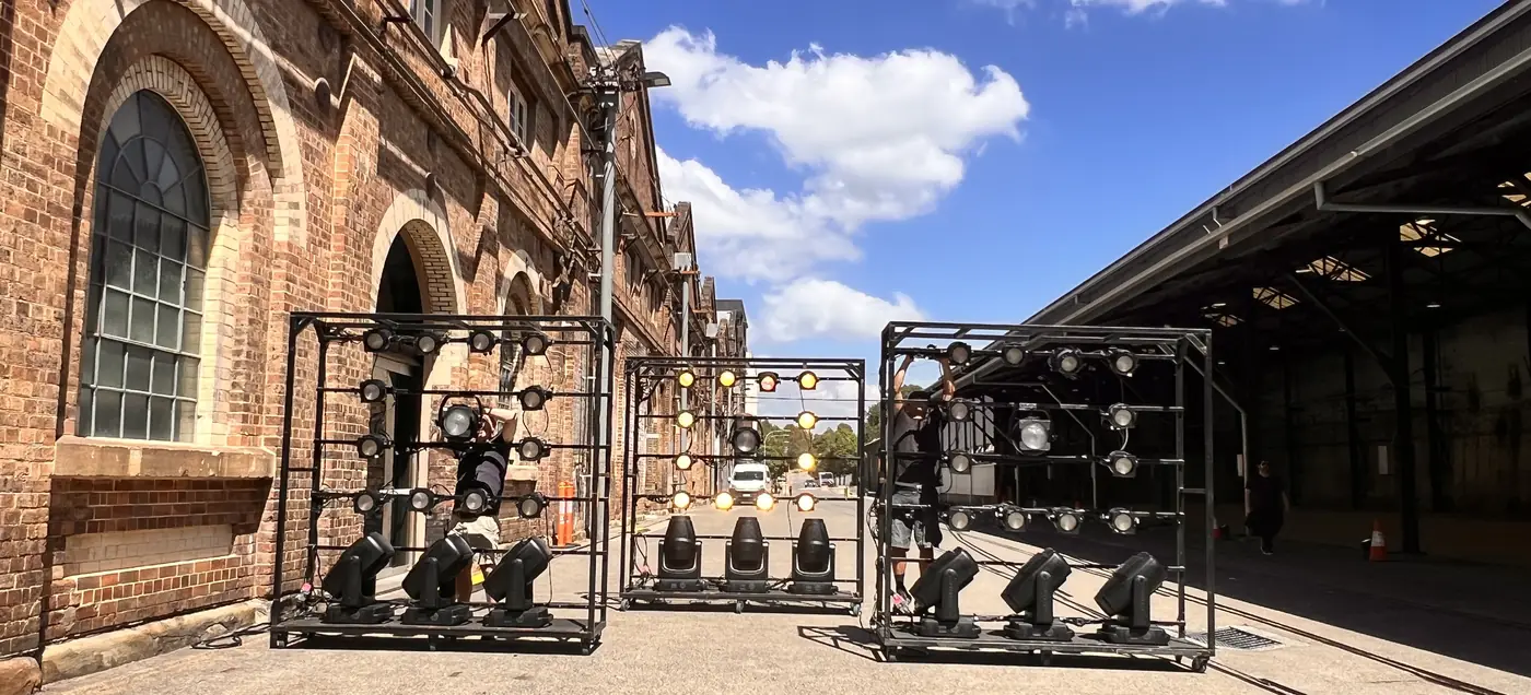 Moving-light rigs on frames in a sunlit studio yard